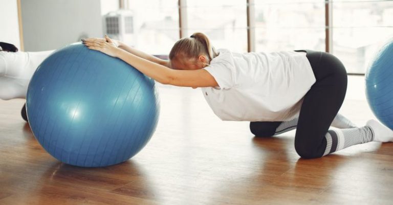 Healthcare Future - Side view of female sportswoman while group training with fitness ball during prenatal workout with crop friend in modern gym during daytime