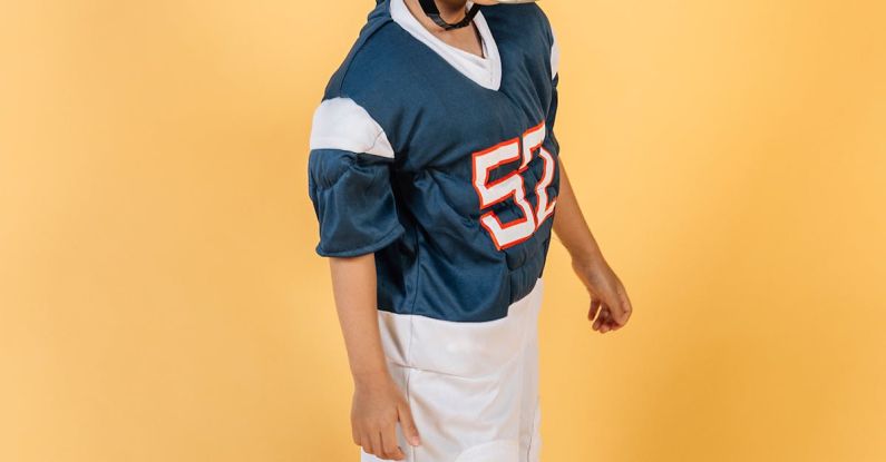 Future Skills - Full length Asian boy in American football player uniform with number and helmet standing in studio on yellow background and looking away
