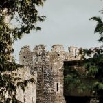 Remote Culture - Exterior of aged stone castle located behind lush green trees under gray gloomy sky