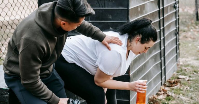 Trust Transparency - Sportsman clapping shoulder of plump tired female trainee sitting near net fence with bottle of water after training in autumn park