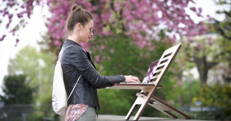 Workplace Flexibility - Woman in Leather Jacket Standing on a Park while Working on Her Laptop