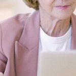 Career Transition Brand - Aged female in eyeglasses with cup checking important documents on netbook on blurred background