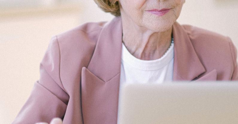 Career Transition Brand - Aged female in eyeglasses with cup checking important documents on netbook on blurred background