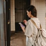 Online Platform - Side view of young concentrated ethnic female in casual clothes and backpack browsing mobile phone while standing on platform of subway station