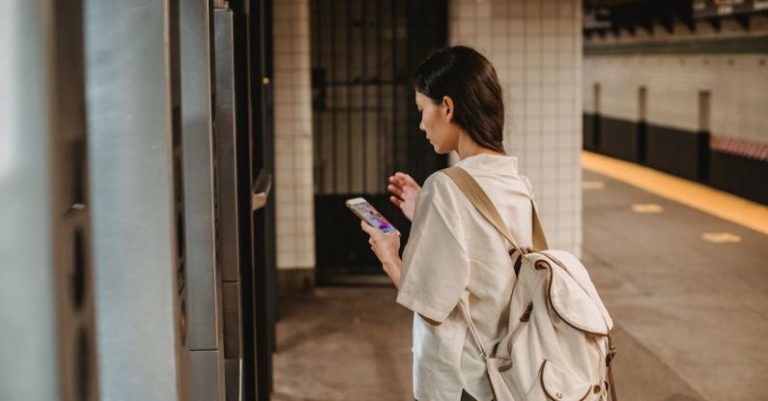 Online Platform - Side view of young concentrated ethnic female in casual clothes and backpack browsing mobile phone while standing on platform of subway station
