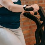 Persistence Motivation - Side view of cheerful plus size ethnic female in activewear with towel exercising on fitness equipment during workout in gym