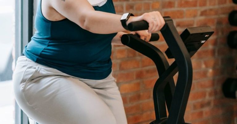 Persistence Motivation - Side view of cheerful plus size ethnic female in activewear with towel exercising on fitness equipment during workout in gym