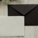 Cover Letter Spotlight - Top view of blank black envelope with white card placed on table with pencil and dry green sprig in modern room