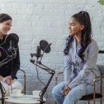 Interview Confidence - Diverse women communicating while recording voice in studio with white brick walls in daytime