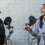 Remote Interview - Smiling African American female guest gesticulating while having interview with journalist sitting near mic