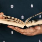 Course Selection - Anonymous male in dark tee shirt reading interesting book while standing in front of light wall