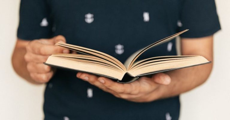 Course Selection - Anonymous male in dark tee shirt reading interesting book while standing in front of light wall