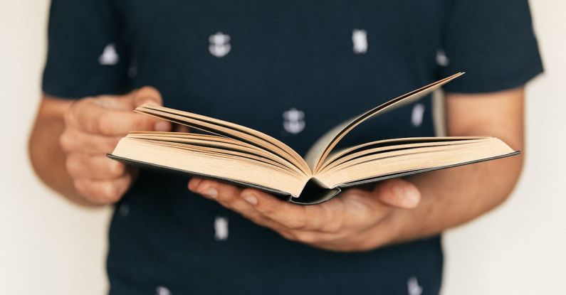 Course Selection - Anonymous male in dark tee shirt reading interesting book while standing in front of light wall